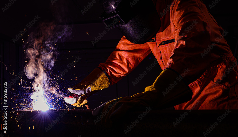 Man worker wearing fire protective mask and fire protection gloves with personal protection equipment standing steel box welding