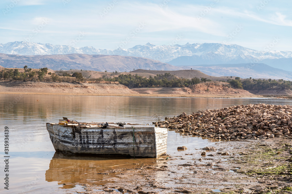 Wooden boat on the shore of Takerkoust lake with Atlas mountains in the background, Morocco