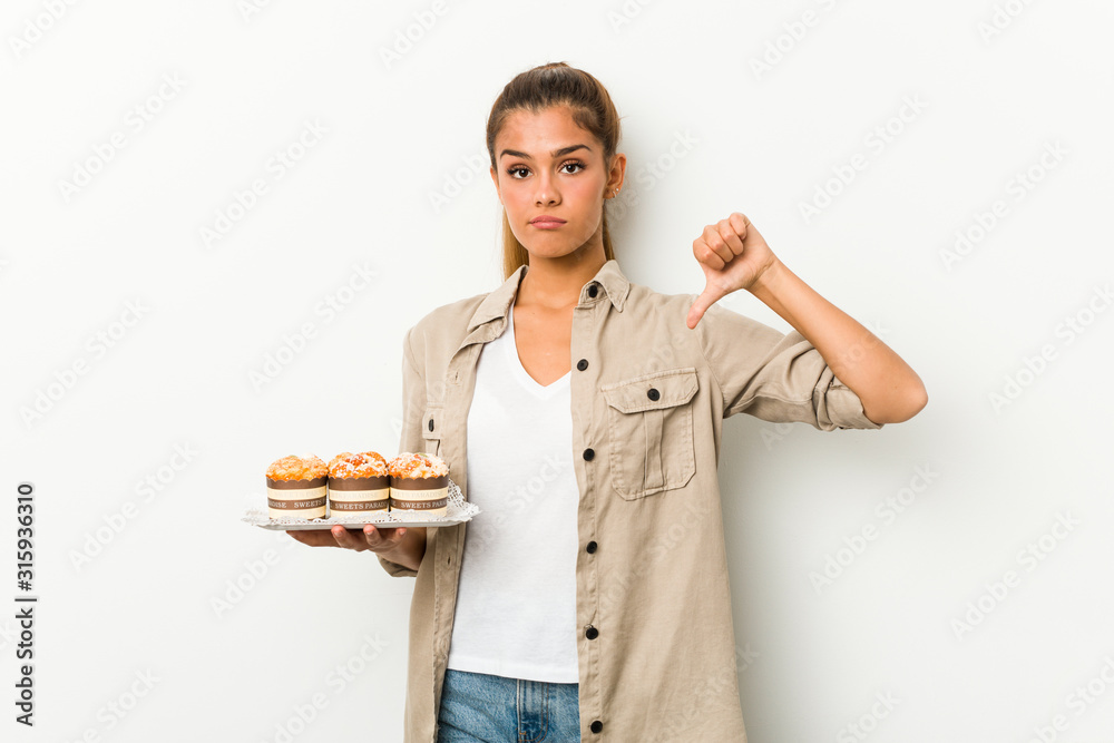 Young caucasian woman holding sweet cakes showing a dislike gesture, thumbs down. Disagreement concept.