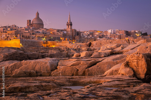 Rocky coast of Malta and the architecture of Valletta city at dawn.