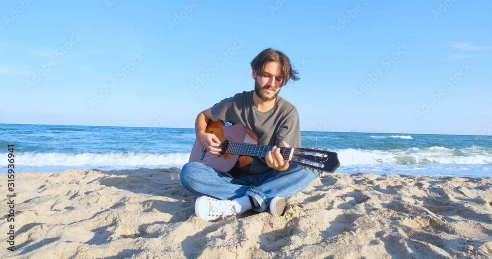 Young handsome male play in acoustic guitar on the beach in sunny day, sea or ocean on background 4K UHD	
