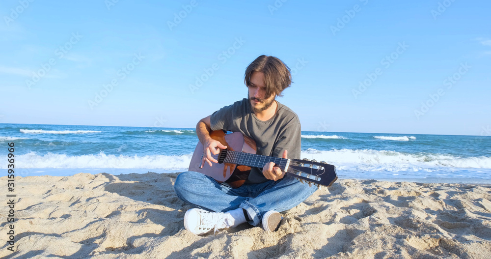Young handsome male play in acoustic guitar on the beach in sunny day, sea or ocean on background 