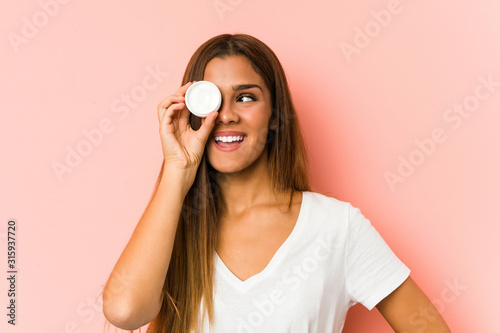 Young caucasian woman holding a mousturizer isolated on a pink background