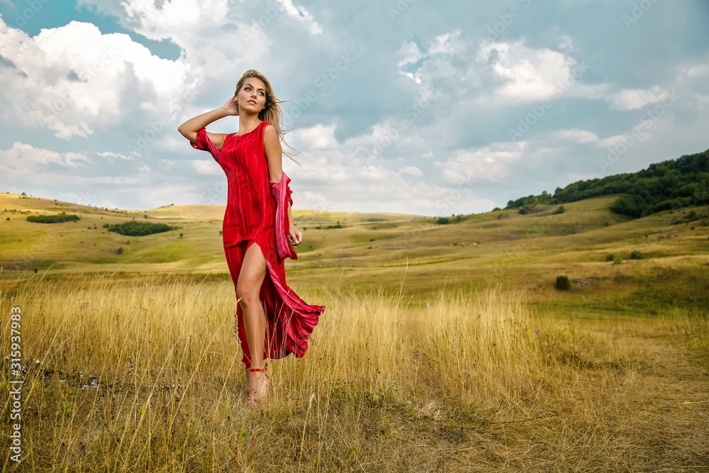 Obraz premium Beautiful young blonde enjoys walking through grass in summer
