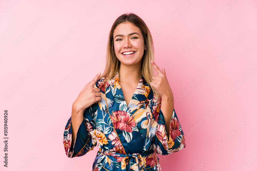 Young caucasian woman wearing pajamas smiles, pointing fingers at mouth. Young caucasian woman wearing pajamas smiles, pointing fingers at mouth.