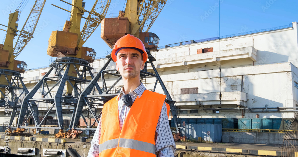 male worker of sea harbor in orange helmet and safety west, cranes and sea background male worker of sea harbor in orange helmet and safety west, cranes and sea background