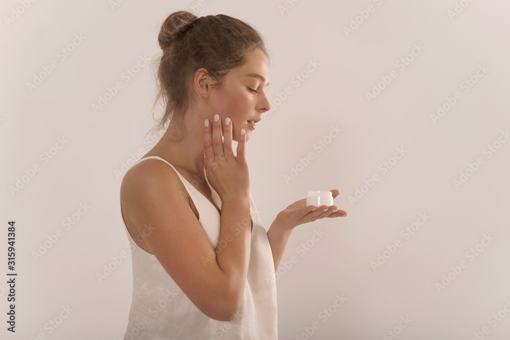 Portrait of a young attractive happy woman with a jar of cream in her hands.