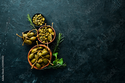 Capers. Marinated capers in a bowl on a black stone background. Top view. Free space for your text. photo