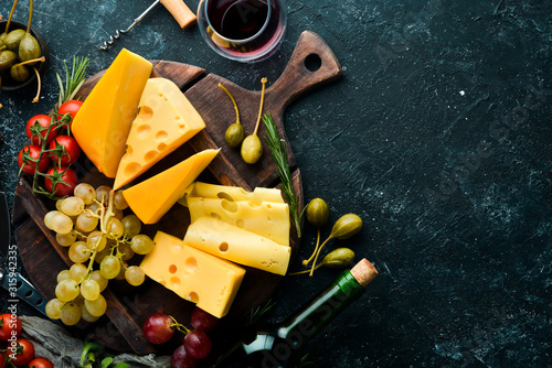 Wine, cheese and snacks on a black stone background. Assorted cheese. Top view. Free space for your text.