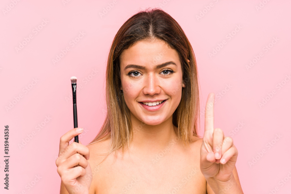 Young caucasian woman holding a eyebrush isolated showing number one with finger. Young caucasian woman holding a eyebrush isolated showing number one with finger.