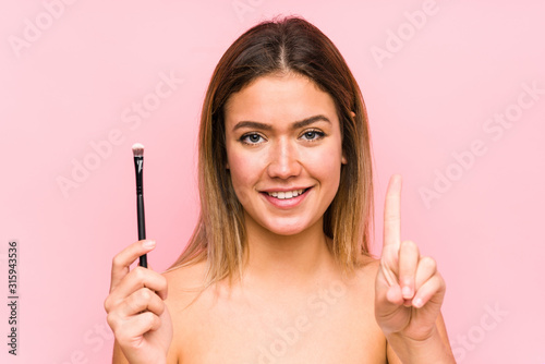 Young caucasian woman holding a eyebrush isolated showing number one with finger.