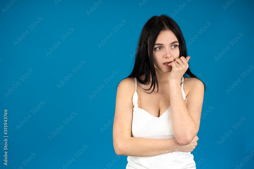Nervous brunette woman biting fingers isolated on blue background