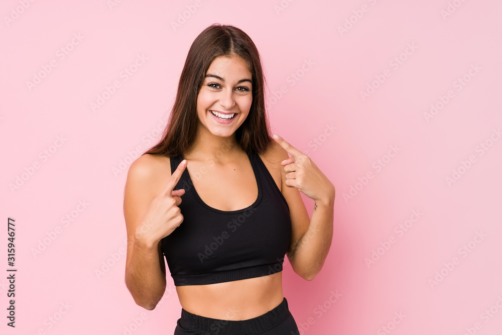 Young caucasian fitness woman doing sport isolated smiles, pointing fingers at mouth.