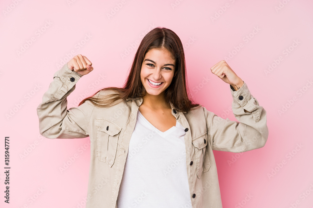 Young caucasian woman posing in a pink background showing strength gesture with arms, symbol of feminine power Young caucasian woman posing in a pink background showing strength gesture with arms, symbol of feminine power