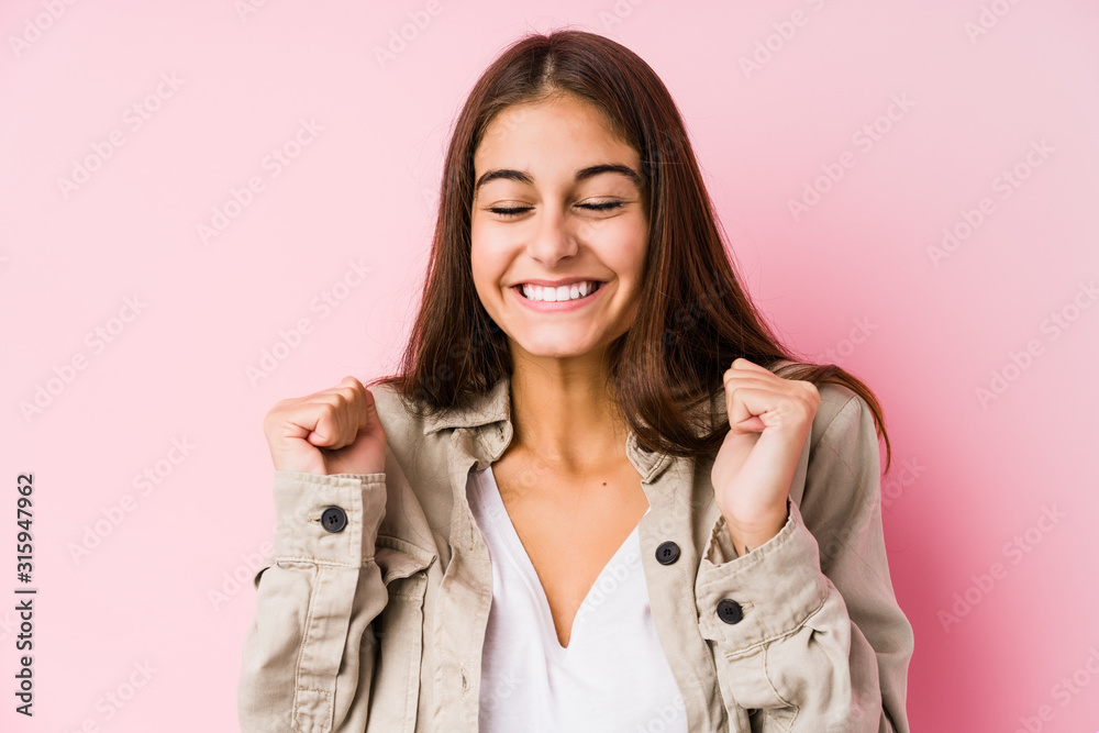 Young caucasian woman posing in a pink background raising fist, feeling happy and successful. Victory concept. Young caucasian woman posing in a pink background raising fist, feeling happy and successful. Victory concept.