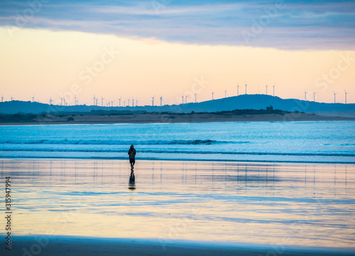 Silhouette of man walking on sunset beach with windmills on background in Essaouira, Morocco