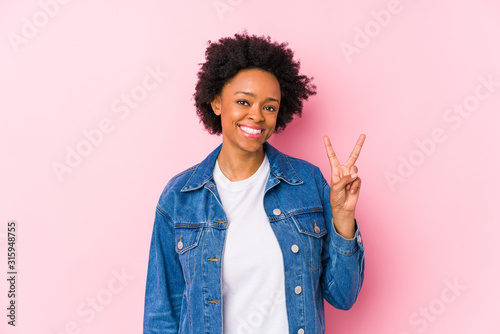 Young african american woman against a pink backgroound isolated showing victory sign and smiling broadly.