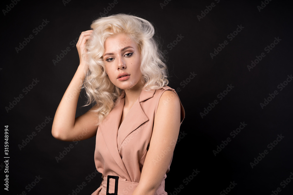 Naklejka premium Stylish blonde woman touching hair isolated on black background