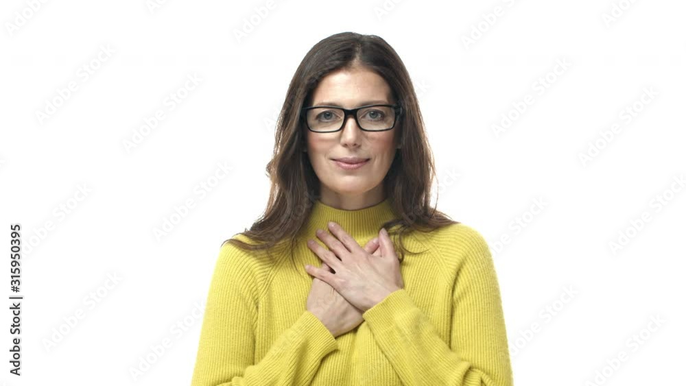 Slow-motion tender and touched, lovely hopeful adult woman, middle-aged mother in glasses, holding hands on heart, smiling happy and look down, praying, having dearest in her mind Slow-motion tender and touched, lovely hopeful adult woman, middle-aged mother in glasses, holding hands on heart, smiling happy and look down, praying, having dearest in her mind
