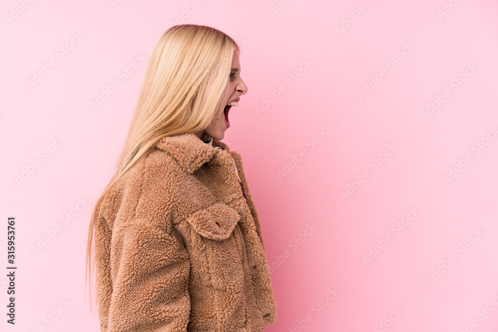 Young blonde woman wearing a coat against a pink background shouting towards a copy space Young blonde woman wearing a coat against a pink background shouting towards a copy space