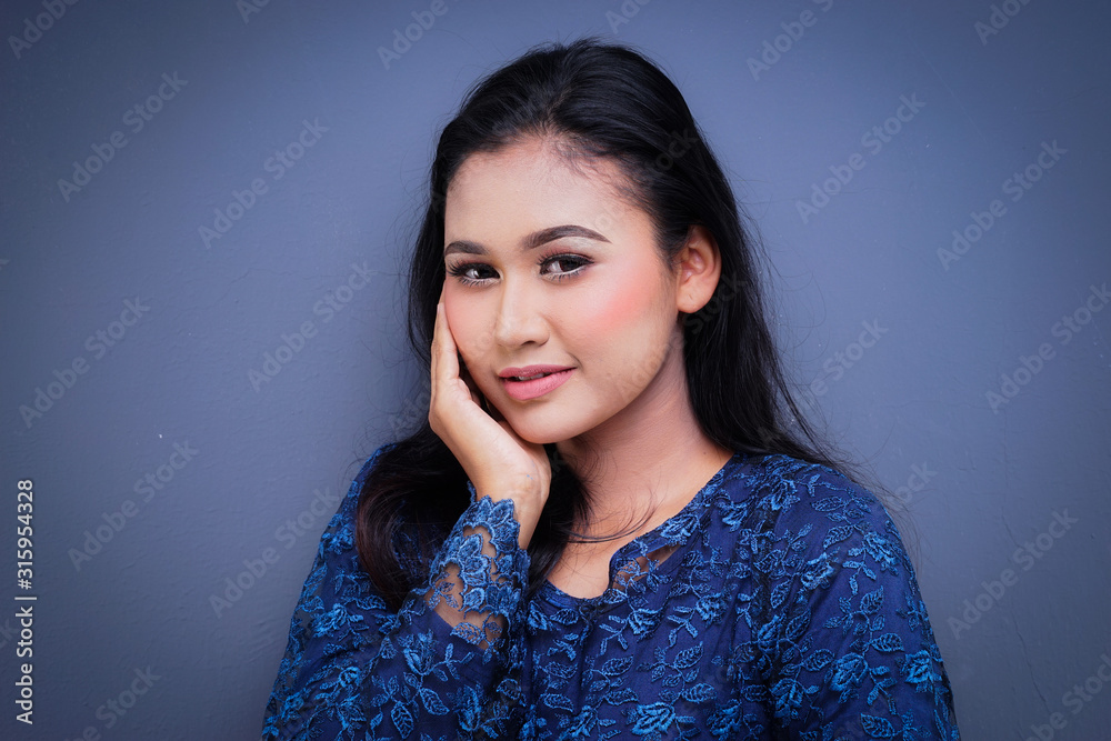 Closeup of a beautiful female Muslim model wearing dark blue modern kurung, a modern urban lifestyle apparel for Muslim women isolated on grey background. Beauty and fashion concept. Closeup of a beautiful female Muslim model wearing dark blue modern kurung, a modern urban lifestyle apparel for Muslim women isolated on grey background. Beauty and fashion concept.