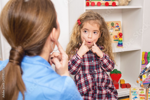 Young girl  in speech therapy office. Preschooler exercising correct pronunciation with speech therapist.