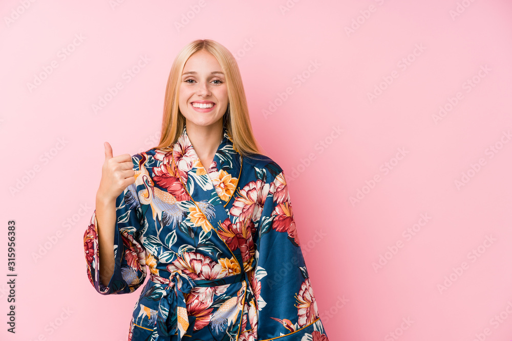 Young blonde woman wearing a kimono pajama smiling and raising thumb up Young blonde woman wearing a kimono pajama smiling and raising thumb up