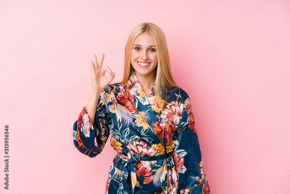 Young blonde woman wearing a kimono pajama cheerful and confident showing ok gesture. Young blonde woman wearing a kimono pajama cheerful and confident showing ok gesture.