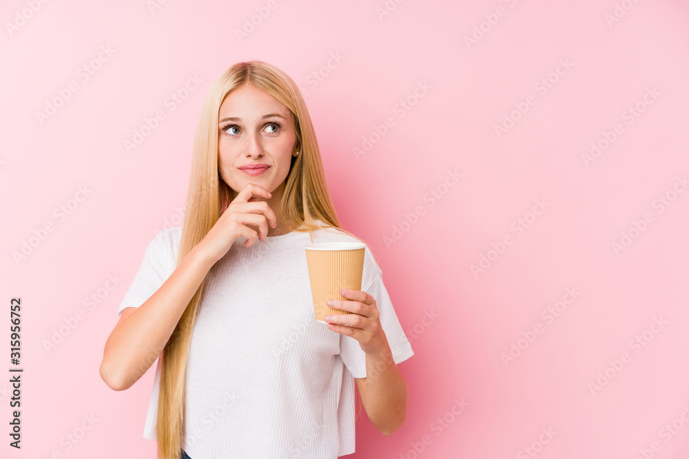 Young blonde girl holding a takeaway coffee looking sideways with doubtful and skeptical expression. Young blonde girl holding a takeaway coffee looking sideways with doubtful and skeptical expression.