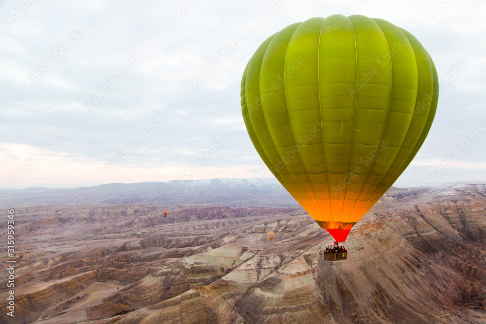 Huge green hot air balloon flying over the famous tourist place Cappadociaat at winter time