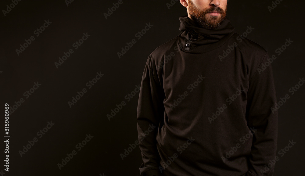 A guy without a face in a black tracksuit on a black background. A man model with a beard and mustache stands confidently in the frame.