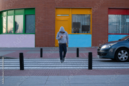 Distracted Caucasian boy looking at his cell phone passes a crosswalk, a car stops and gives way. Concept technology.