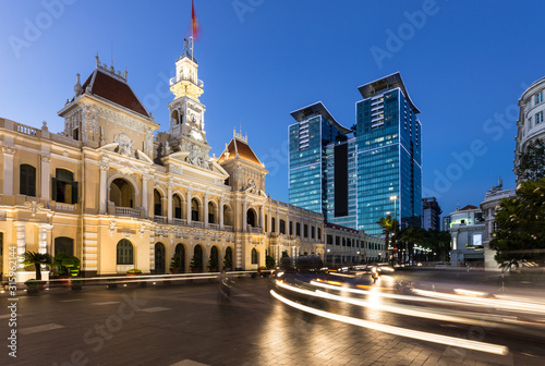 Traffic rushing at night in front of the famous People's comittee building, which contrasts with modern tower, in Ho Chi Minh city in Vietnam largest, city, aka Saigon.