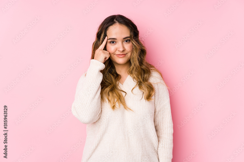 Young curvy woman posing in a pink background isolated pointing temple with finger, thinking, focused on a task.