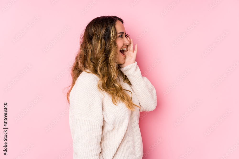 Young curvy woman posing in a pink background isolated shouting and holding palm near opened mouth. Young curvy woman posing in a pink background isolated shouting and holding palm near opened mouth.