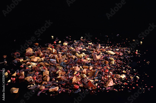 Fruit tea with dry ginger, rose hip, pink pepper, apple, cinnamon, flower petals on black background. Front view, copy space.