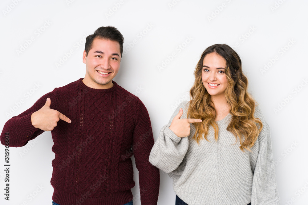 Young couple posing in a white background person pointing by hand to a shirt copy space, proud and confident Young couple posing in a white background person pointing by hand to a shirt copy space, proud and confident