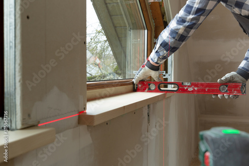 home improvement handyman installing window sill in new build attic by using leveler and laser leveler