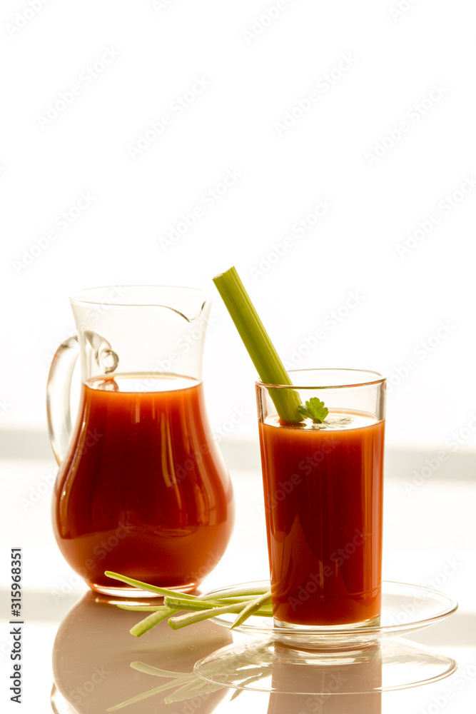Tomato juice in a jug and a glass with celery, on a white background, close-up Tomato juice in a jug and a glass with celery, on a white background, close-up
