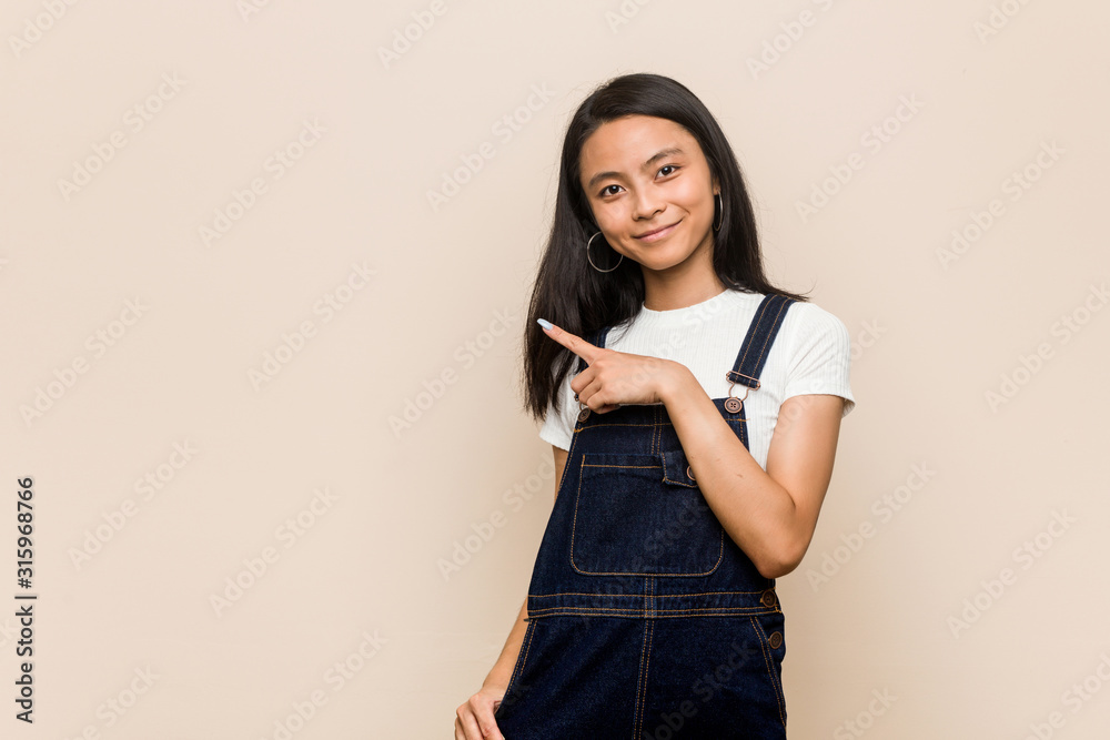 Young cute chinese teenager Young blonde woman wearing a coat against a pink background smiling and pointing aside, showing something at blank space. Young cute chinese teenager Young blonde woman wearing a coat against a pink background smiling and pointing aside, showing something at blank space.