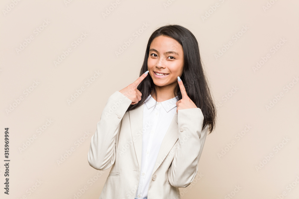 Young business chinese woman smiles, pointing fingers at mouth. Young business chinese woman smiles, pointing fingers at mouth.