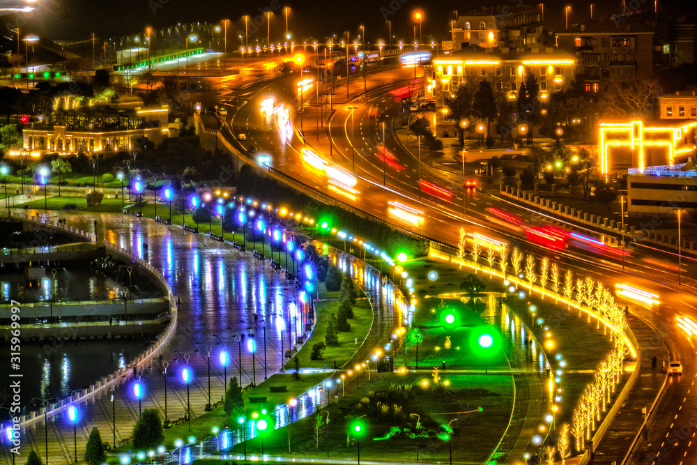 modern city night lights of seashore park and highway motion car traffic landmark against black sky background. Closeup view of Baku city Azerbaijan skyline landscape at dark at winter time