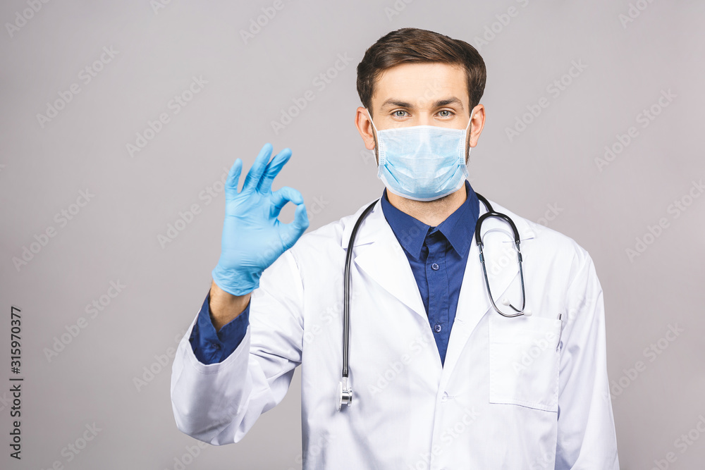Portrait of young doctor in mask and blue gloves ok sign isolated on grey background. Portrait of young doctor in mask and blue gloves ok sign isolated on grey background.