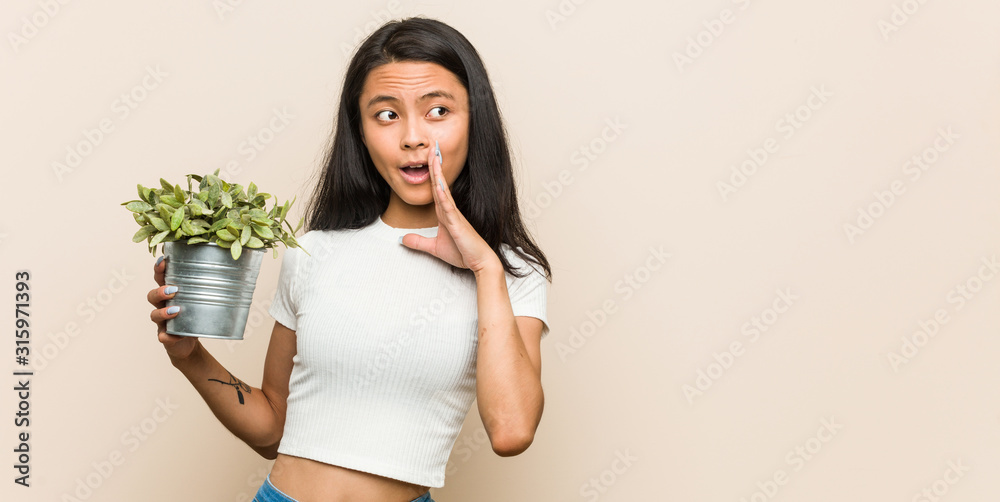 Young asian woman holding a plant is saying a secret hot braking news and looking aside Young asian woman holding a plant is saying a secret hot braking news and looking aside