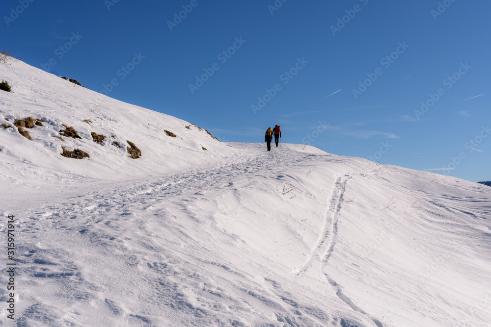 Personen auf Weg im Schnee in den Alpen vor blauem Himmel