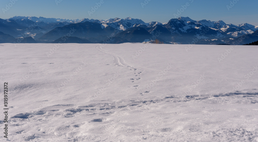 Spuren im Schnee bei blauem Himmel vor Begkulisse