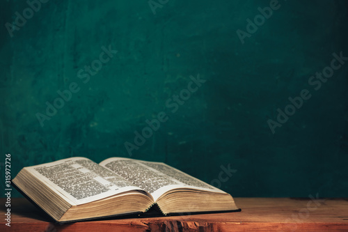 Open bible on a red old wooden table. Beautiful green wall background.