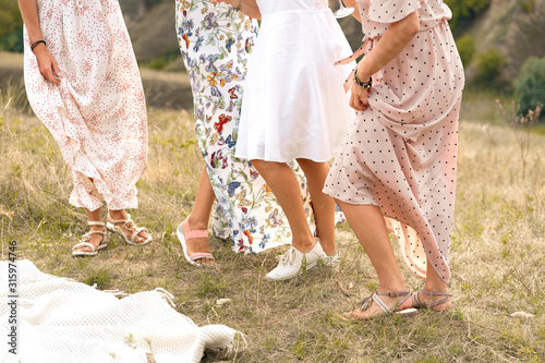 The company of female friends having fun, dancing on summerfield in long dresses showing their legs. Summer rural style picnic concept. photo