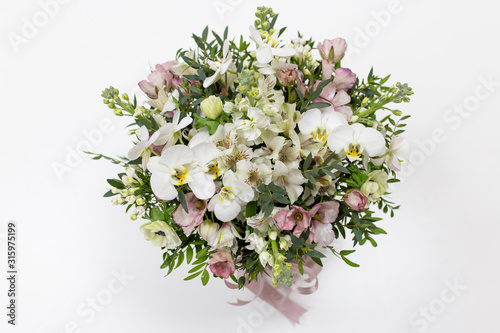Gorgeous flower arrangement in a round hat box with a satin ribbon on a light background (color: white, pink, green. Flowers: phalaenopsis, alstroemeria, anemone, pistachio leaves)
