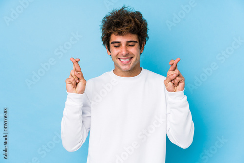 Young caucasian man against a blue background isolated crossing fingers for having luck